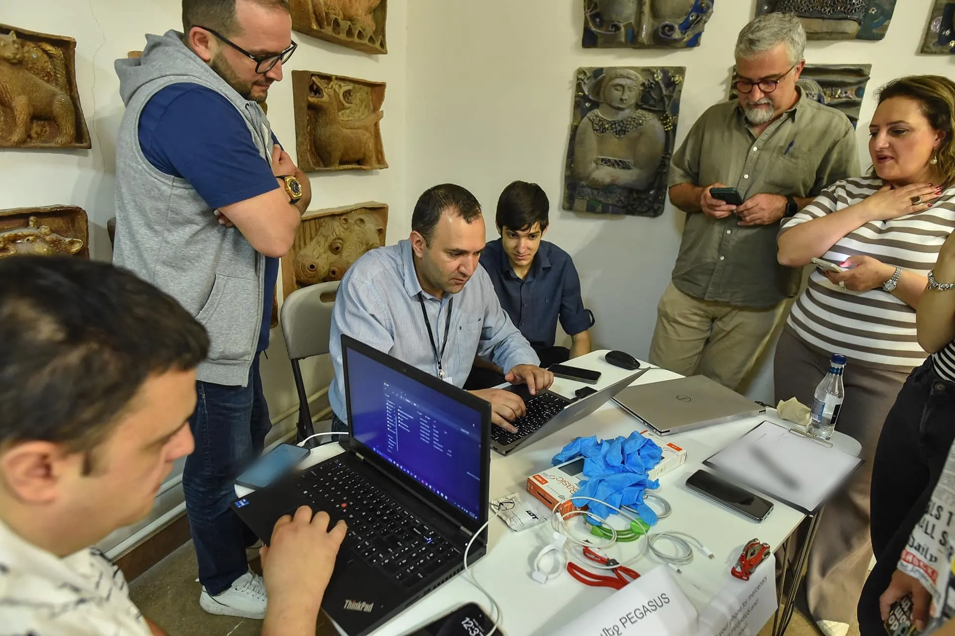 Phones being checked for Pegasus spyware: people wait with their phones while laptops run the analysis.